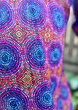 A close-up of the colorful garment featuring a repeating circular dot pattern in purple, blue, pink, and orange tones, with a blurred outdoor background visible on the right.