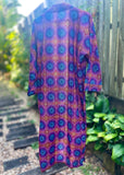 Kimono back with a vibrant purple, blue, and orange geometric pattern, hanging outdoors against a wooden fence and garden background.