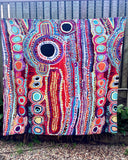 A vibrant, multicolored tablecloth featuring an intricate pattern, hanging outdoors on a clothesline in front of a wooden fence.