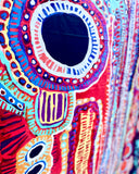 A close-up of the highly colourful, patterned textile featuring intricate circular and abstract geometric designs in red, blue, yellow, purple, and white.