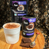 Oxfam Fair drinking chocolate with a cup of hot chocolate on a wooden surface.